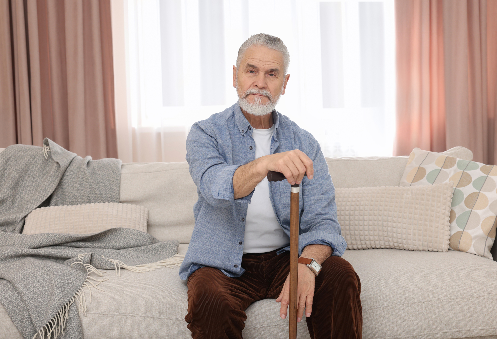 Senior man with walking cane sitting on sofa at home